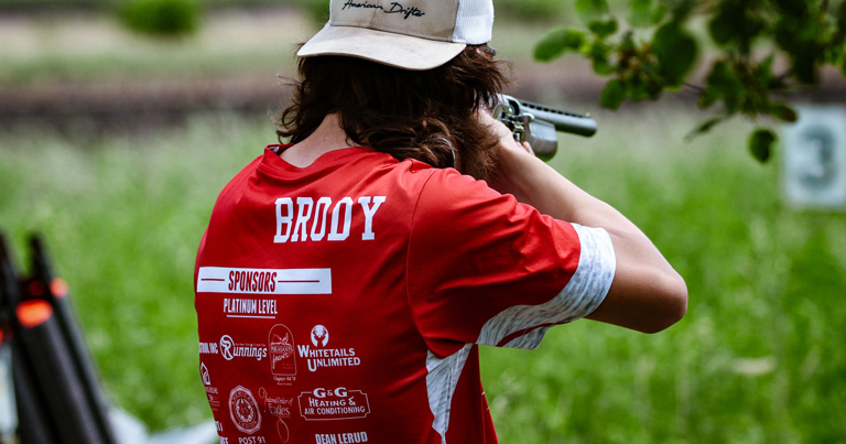 A man in a red shirt is shooting a rifle.
